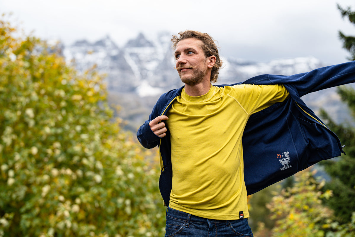 A man wearing a yellow long-sleeve top putting on a navy blue fleece
